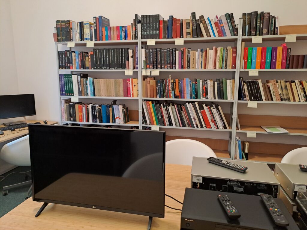 Reading Room of the National Institute of Music and Dance, computer and DVD and VHS recorder on a desk in front of book shelves.